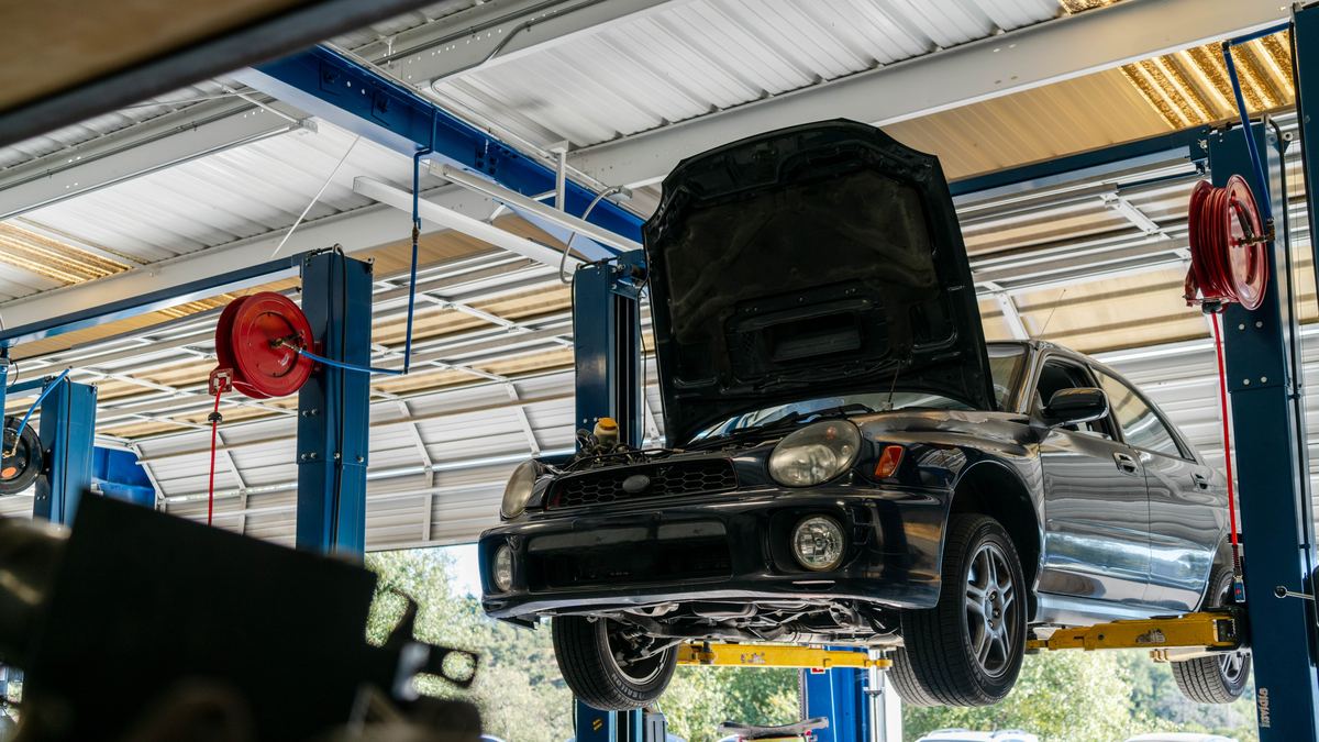 A car up on a two-post lift with the hood open in a working service bay.
